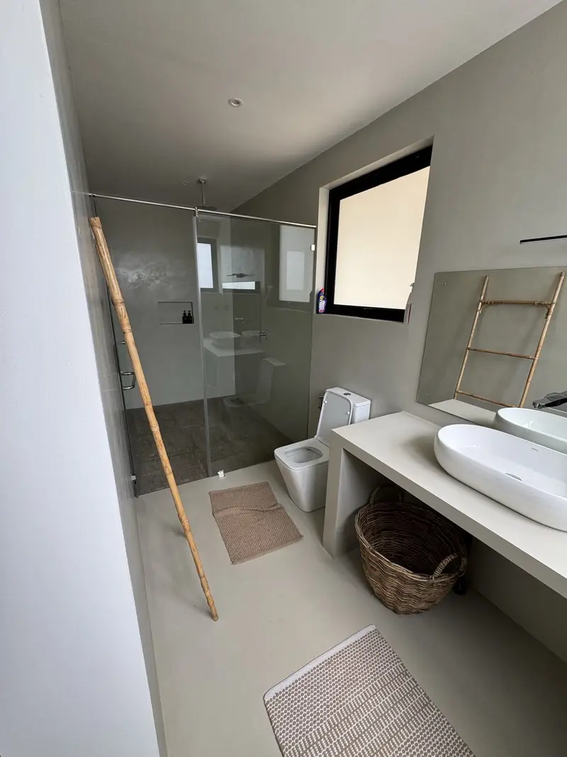 The open bathroom: bare concrete, a walk-in shower, cane and jute