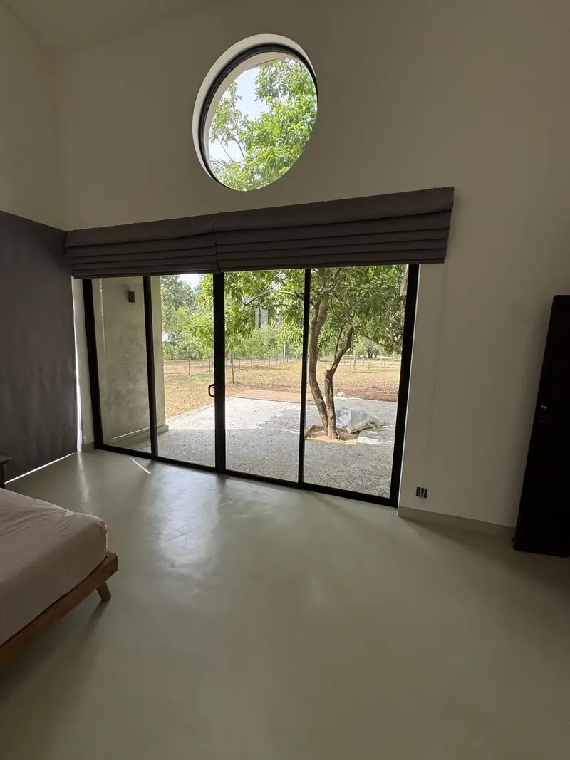 A round window and a wall of glass opening onto a lone tree and the fields